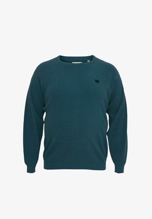 Tamsiai mėlyna megzta palaidinė su apvalia iškirpte, raukšlėta tekstūra ir raglaninėmis rankovėmis. Priekyje kairėje pusėje yra mažas juodas logotipas.