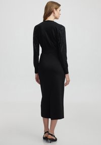 Schwarzes Midi-Kleid mit langen Ärmeln und Paillettenakzenten, einem taillierten Oberteil und einem geraden Rock mit einem dezenten Schlitz hinten.