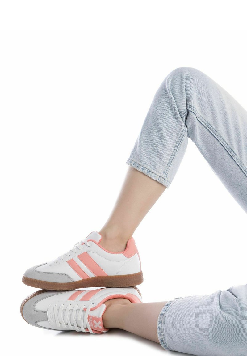 Zapatillas blancas con acentos rosas, que presentan punteras de ante gris y una suela de goma texturizada. Combinadas con unos jeans de mezclilla claros y doblados.