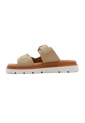 Sandale beige style mule avec deux larges brides et une boucle, semelle intérieure marron rembourrée et semelle épaisse blanche avec rainures.