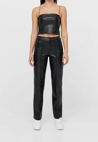 Zwarte cropped tanktop van leer, gecombineerd met high-waisted leren broek, met rechte pijpen en minimale stikdetails.
