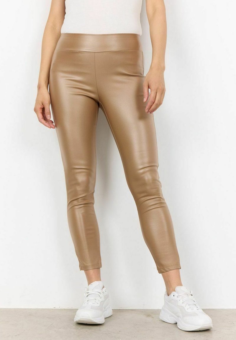 Tan neplederen leggings met een hoge tailleband, slim fit en enkellang, gecombineerd met witte sneakers op een neutrale achtergrond.