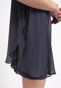 Robe en chiffon bleu marine avec un design fluide, des volants superposés à l'ourlet, une texture semi-transparente et une silhouette décontractée.