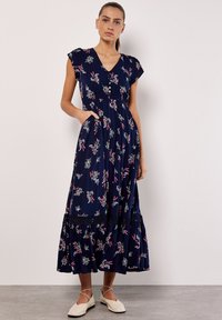 Vestido maxi floral en navy con mangas de capucha, escote en V, cintura fruncida y falda de volantes. Incluye bolsillos y un dobladillo con encaje.