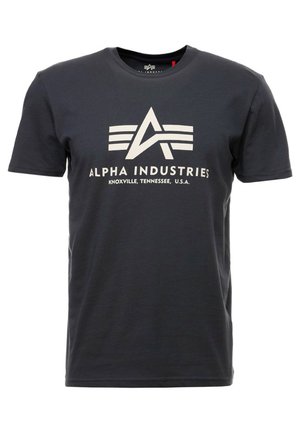 T-paita tummanharmaasta puuvillasta, jossa on lyhyet hihat. Sisältää suuren valkoisen logon, jossa on kolme raitaa ja teksti "ALPHA INDUSTRIES, KNOXVILLE, TENNESSEE, U.S.A."