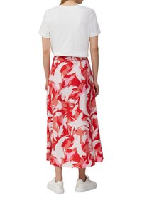 T-shirt en coton blanc associé à une jupe fluide rouge ornée d'un motif abstrait de plumes blanches. Complété par des baskets blanches.