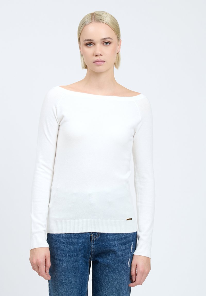 Witte lange mouwen shirt met een bootnek, geribbeld zoom en een gladde textuur. Gecombineerd met versleten blauwe jeans.