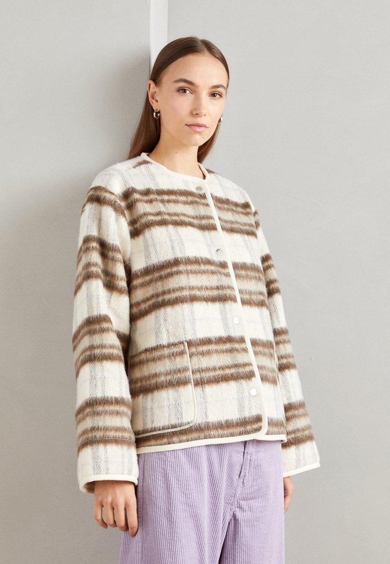 Knappjakke i kremfarge med brun stripemønster, laget av mykt stoff. Har rund hals, lange ermer og sidelommer.