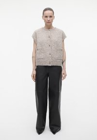 Lichtbeige, textuurgebreide top met korte mouwen, grote knopen en twee voorzakken. Gecombineerd met high-waisted, loose-fitting zwarte leren broek.