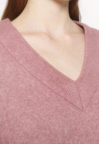 Ljust rosa v-ringad tröja i mjukt stickat material, med ribbade kanter och en avslappnad passform som framhäver en slät textur.
