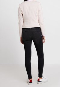 Veste en similicuir rose clair à coupe ajustée, associée à un jean skinny noir. Les baskets blanches comportent des accents rouges et noirs sur le talon.