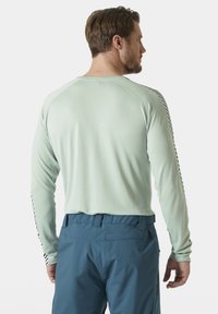 Licht mintkleurig shirt met lange mouwen en een textuurpatroon, met zwarte gestreepte accenten op de mouwen. Gecombineerd met blauwe broek.