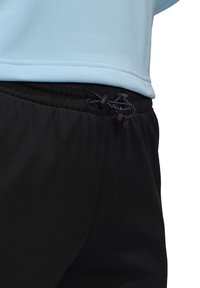 Haut de sport bleu clair associé à un pantalon de jogging noir avec une taille élastique, des détails à cordons et une texture de tissu lisse.