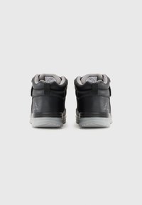 Un par de zapatillas altas en negro y gris con logos de marca en la parte trasera y cuellos acolchados, mostradas desde atrás sobre un fondo blanco.