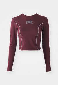 Bordeaux pitkähihaisessa crop-topissa, joka on valmistettu joustavasta kankaasta, on valkoiset kontrastiväriset tikkaukset ja Nike-logo rinnassa. Hihoissa on tiukka istuvuus.
