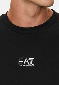 T-shirt in cotone nero. Collo rotondo con una texture morbida. Presenta il logo bianco EA7 Emporio Armani sul petto.