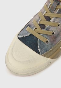 Texturált bézs orr-résszel rendelkező sportcipő, többszínű szövetfelsőrésszel, amely kék, szürke és barna árnyalatokat tartalmaz, valamint világoszöld fűzőkkel. Foszló szövet széllel.