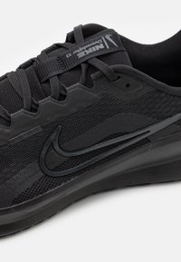 Musta Nike urheilujalkine, jossa on verkkomateriaali, rakennekoristeet, näkyvä swoosh-logo ja pehmustettu pohja.