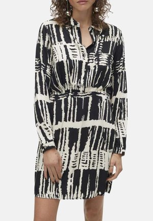 Robe à motif noir et blanc avec des manches longues, un col et une taille cintrée. Tissu lisse avec des rayures et des formes abstraites.