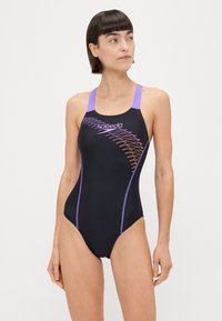 Črn kopalni kostim s vijoličnimi poudarki, ki vsebuje zig-zag vzorec po strani. Narejen iz gladkega materiala z hrbtom v stilu racerback. Prikazana je blagovna znamka Speedo.