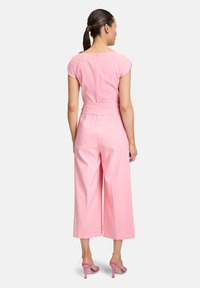 Tuta rosa con maniche corte, design a gamba larga, vita aderente e chiusura con zip sul retro. Abbinata a scarpe con tacco alto rosa.