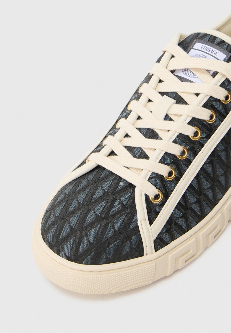 Schwarzer Sneaker mit Muster, beigen Schnürsenkeln, goldenen Ösen und einer strukturierten Gummisohle. Verfügt über ein geometrisches Design auf dem Obermaterial.