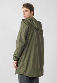 Giacca impermeabile verde oliva con cappuccio, polsini regolabili e orlo posteriore più lungo per una maggiore copertura. Materiale liscio e leggero.