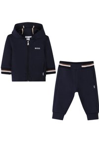 Das marineblaue Trainingsanzug-Set besteht aus einer Kapuzenjacke mit Reißverschluss, einem Logo und gestreiften Akzenten, kombiniert mit passenden Bündchen-Hosen. Hergestellt aus weichem Stoff.