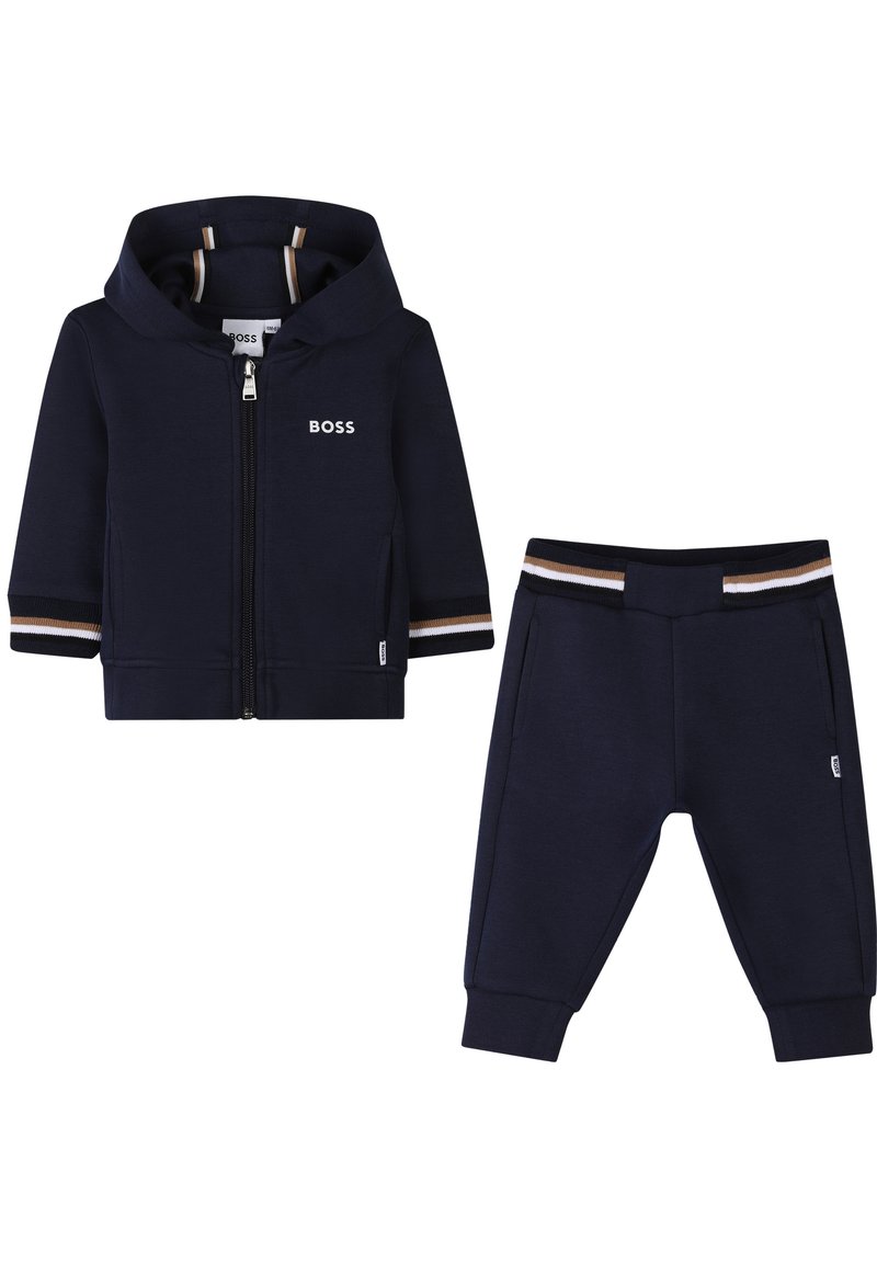 Das marineblaue Trainingsanzug-Set besteht aus einer Kapuzenjacke mit Reißverschluss, einem Logo und gestreiften Akzenten, kombiniert mit passenden Bündchen-Hosen. Hergestellt aus weichem Stoff.