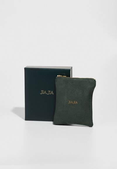 Pungă verde din suede cu fermoar, împodobită cu un logo auriu, așezată lângă o cutie verde închis corespunzătoare. Textură netedă, formă compactă pătrată, design minimalist.
