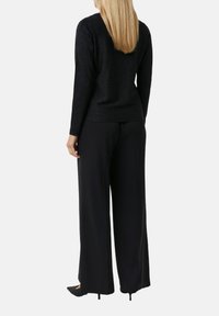 Top nero luccicante a maniche lunghe abbinato a pantaloni larghi neri a vita alta, caratterizzati da una texture liscia e un design semplice ed elegante.