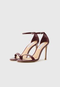 Sandales à talons hauts ouvertes en mauve avec une bride au niveau de la cheville, texture lisse et design à bout carré. Présente un fine talon aiguille et une semelle intérieure rembourrée.