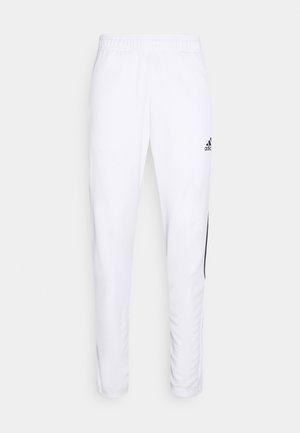 Pantalon de survêtement blanc Adidas avec taille élastique et coupe slim, avec logo Adidas noir sur la cuisse supérieure et bandes latérales noires.