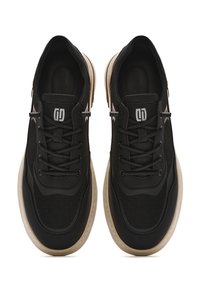 Zapatillas deportivas negras con parte superior de malla y sintético, diseño con cordones, suela de goma y acentos en marrón claro. Presenta el logo cerca de la lengüeta.