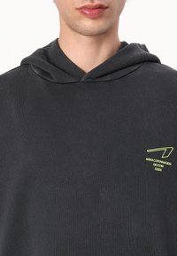 Black hoodie made of soft fabric, featuring a front kangaroo pocket, a drawstring hood, and a small green logo on the chest.