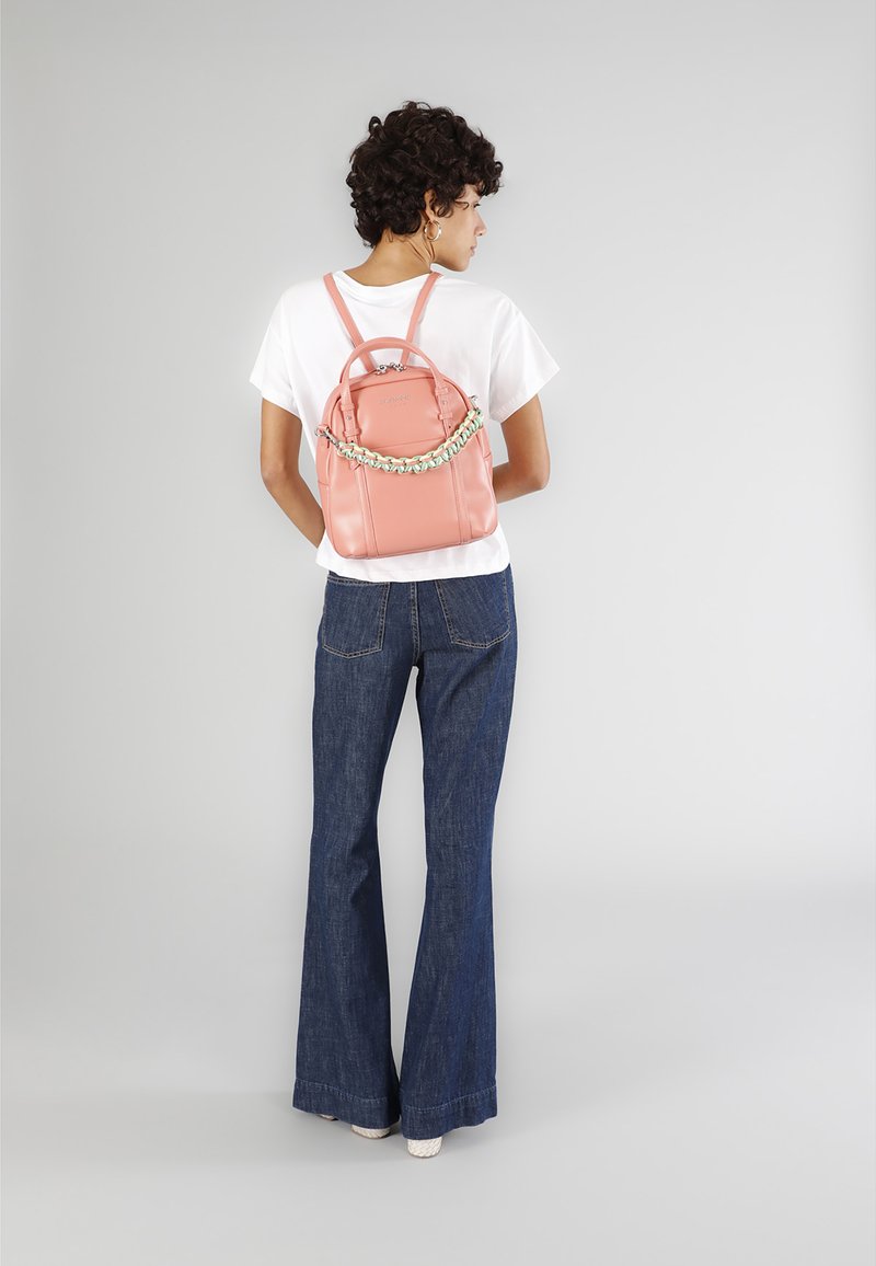 Růžový kožený batoh s látkovým řetězovým akcentem. Má strukturovaný tvar, dvojité ramenní popruhy a horní madlo.