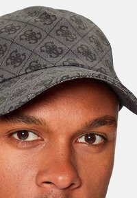 Cappello grigio realizzato in tessuto a motivo con un design del logo scuro. La visiera è curva e la texture sembra intrecciata.