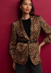 Blazer en tissu doux avec imprimé léopard, doté d'un col cranté, d'une fermeture à un bouton et d'une ceinture noire à la taille, sur un fond bourgogne.