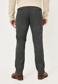 Man wearing dark gray pants, beige long-sleeve shirt, and brown leather shoes, shown from the back against a plain white background.