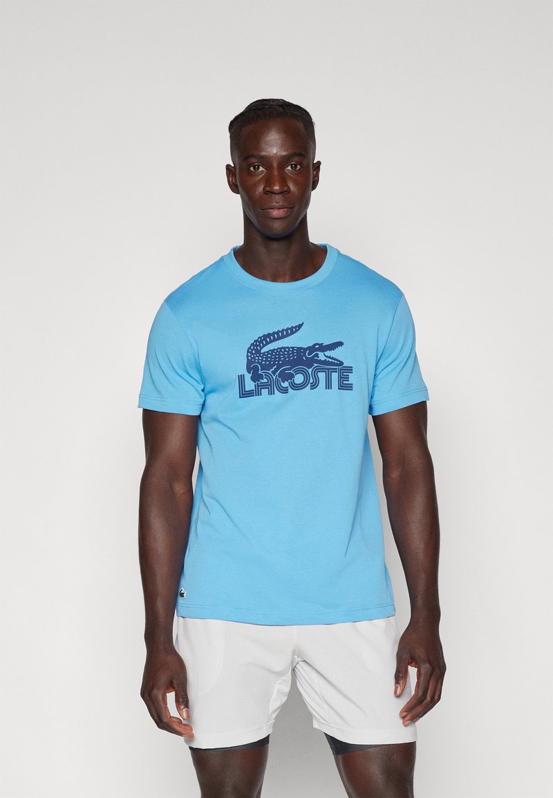 Lichtblauwe crewneck t-shirt van katoen met een marineblauwe krokodil logo en "LACOSTE" tekst, met korte mouwen en een ontspannen pasvorm.