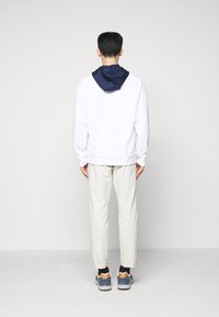 Sudadera con capucha en blanco con capucha azul marino, combinada con pantalones crema. Las zapatillas presentan una paleta de colores en azul marino, gris y naranja.