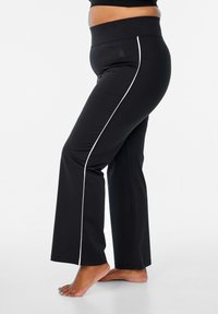 Zwarte flare yoga broek met een brede tailleband, voorzien van witte zijstrepen en een gladde, elastische stoftextuur.
