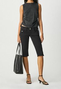 Top negro sin mangas con lazos laterales, jeans cortos negros y bolso negro. El calzado presenta un estampado animal con un tacón bajo.