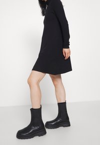Stivali neri in pelle al ginocchio con suola spessa e cerniera laterale, abbinati a un abito nero a maniche lunghe. Design semplice ed elegante.