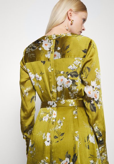 Vestido verde floral com mangas longas, apresentando uma textura de cetim, estampados botânicos, fecho de botão nas costas e um cinto a condizer.