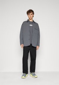 Stripete skjorte i marineblå og hvit, grå grafisk t-skjorte, svarte bukser og flerfargede chunky sneakers med livlige accenter.