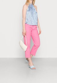 Top azul con estampado y tirantes, pantalones cortos rosas, sandalias de tacón bajo azul claro, sosteniendo un bolso blanco con una cadena como asa.