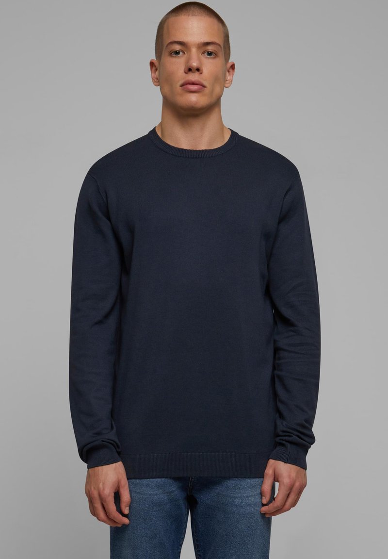 Mørkeblå strikket genser med rund hals og lange ermer, kombinert med blå denim jeans. Slank tekstur, avslappet design.