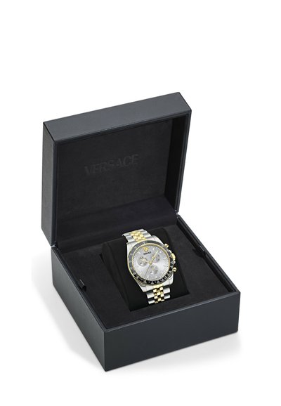 Luksuslik kahetooniline hõbe- ja kuldvärviline käekell kronograafiga, esitatud avatud mustas Versace bränditud kinkekarbis valgel taustal.