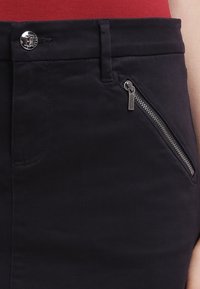 Marineblaue, taillierte Hose mit glatter Textur. Verfügt über einen silbernen Knopf, eine seitliche Reißverschlusstasche mit metallic gezogenem Zugband und Gürtelschlaufen.
